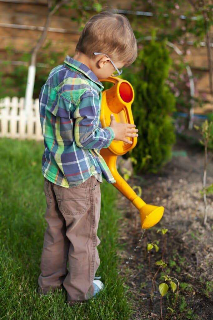 Child watering can watering a garden in the backyard